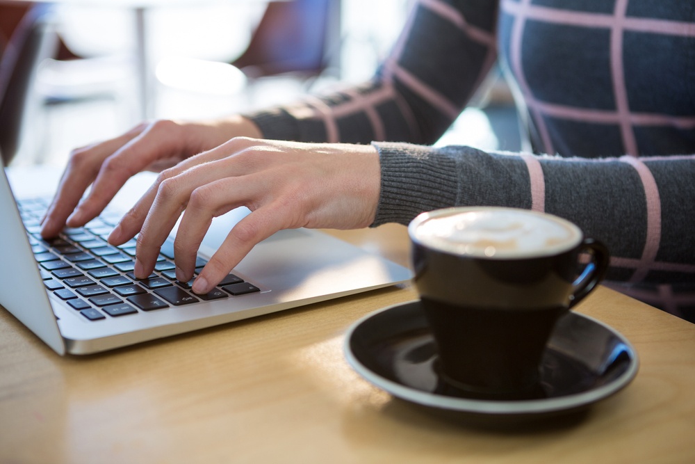 Mid section of woman using laptop with coffee on table in cafeteria